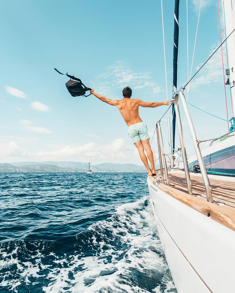 man standing on the side of a sailboat with his arms out