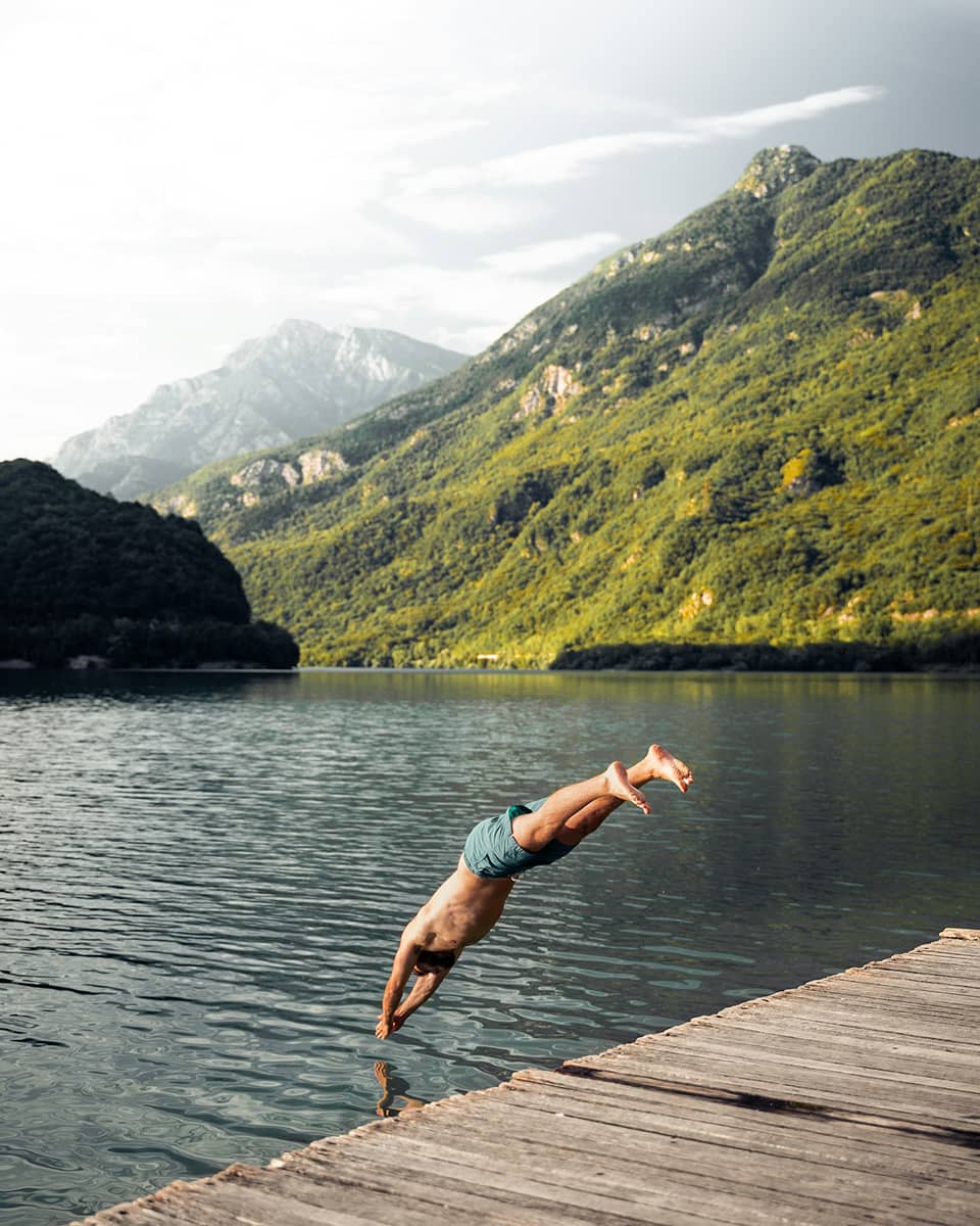man diving in to a lake between mountains