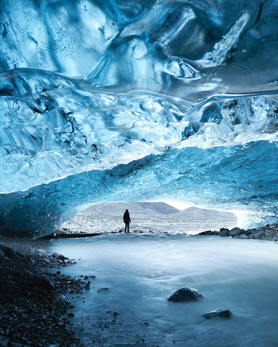man standing inside a crystal blue glacier