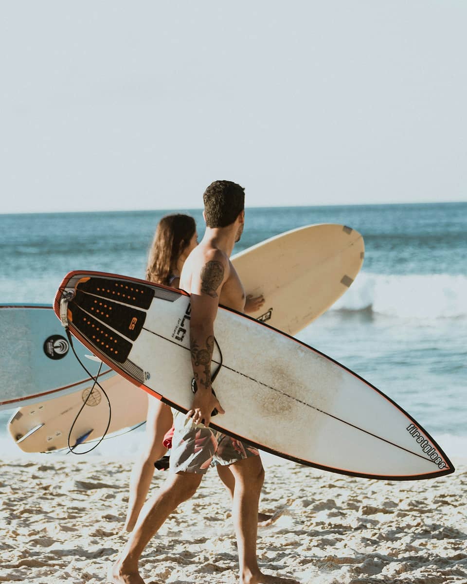 a couple walking down a beach with their surfboards